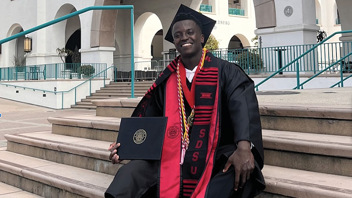 male student in cap and gown poses on steps of student union